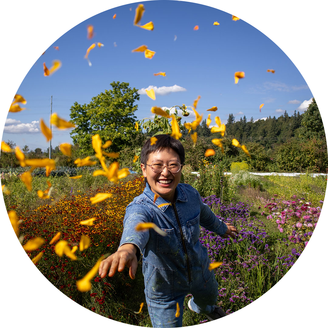 A joyful person tosses yellow flower petals in the air during an immersive workshop at Oxbow Farm & Conservation Center, surrounded by vibrant wildflowers.