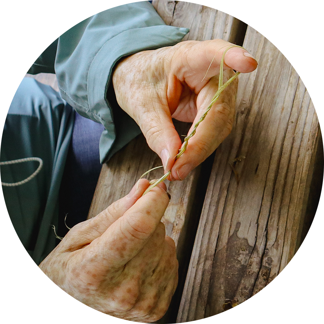 Close-up of hands twisting plant fibers into cordage during a hands-on nature workshop.