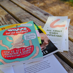 Educational books and pamphlets about worm composting on a wooden table.