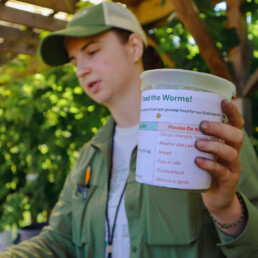 Educator showing a compost bin labeled with food do’s and don’ts for worms.