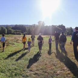 Group of children and adults walking through a sunny field during a nature workshop at Oxbow.