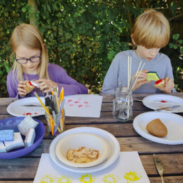Children using cut potatoes to create colorful prints on paper during a workshop.