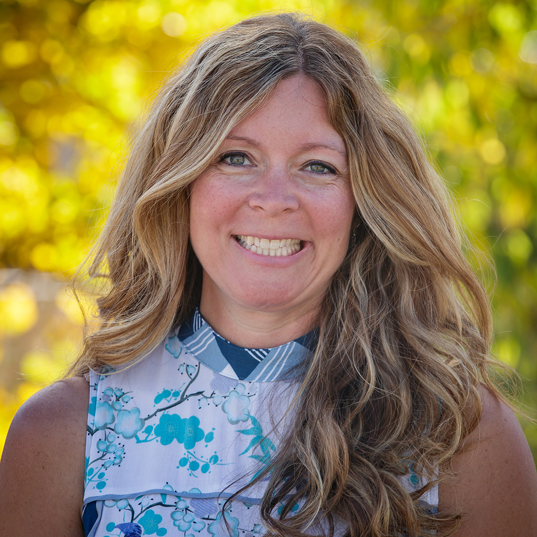 Anne Lowe, Executive Director of Oxbow Farm & Conservation Center, smiling outdoors with golden foliage in the background.