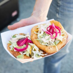 Plate of frybread tacos with cabbage, pickled onions, and sauce from Off the Rez food truck.