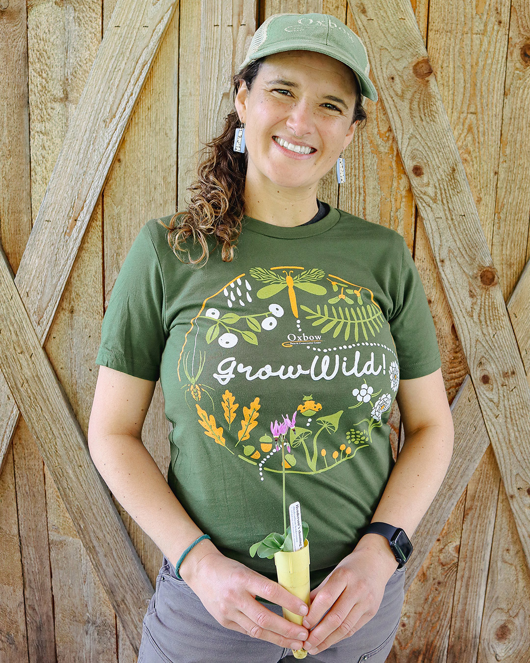 MK wearing Oxbow Grow Wild native plant t-shirt while holding a native plant seedling.