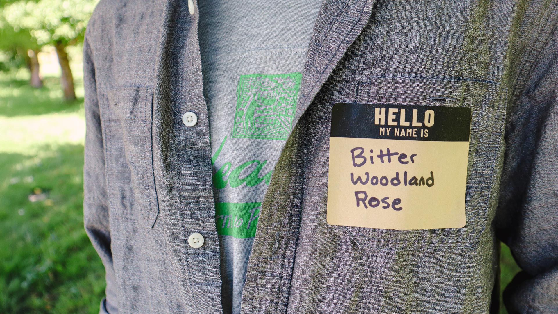 Close-up of a person wearing a handwritten name tag that reads “Bitter Woodland Rose” as part of Oxbow’s PNW Native Plant Name Generator quiz.